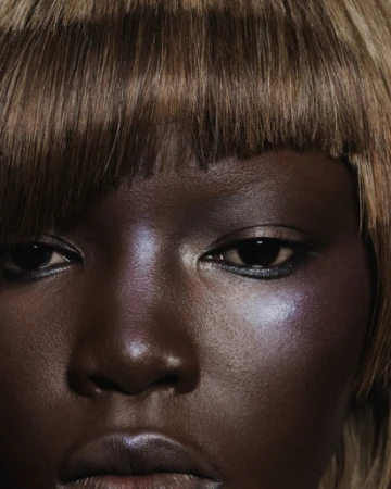 Close-up beauty shot of an African-American woman with an auburn blunt bob, highlighted cheekbones, and glossy lips in a studio setting.
