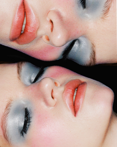 Close-up of two adult females' faces with dramatic make-up in a mirrored effect against a black background in a beauty shot.