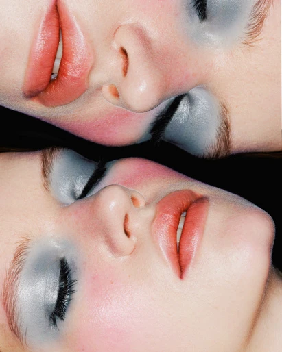 Close-up of two adult females' faces with dramatic make-up in a mirrored effect against a black background in a beauty shot.