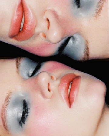 Close-up of two adult females' faces with dramatic make-up in a mirrored effect against a black background in a beauty shot.