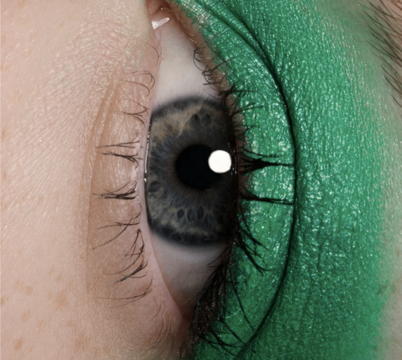 Macro close-up of a blue human eye and eyebrow, surrounded by green eyeshadow.