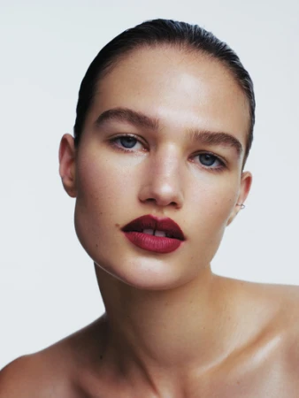 Close-up beauty portrait of a woman with slicked-back dark hair and bold burgundy lipstick against a white background