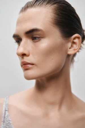 Close-up portrait of a woman with slicked-back hair and a neutral expression against a plain light background