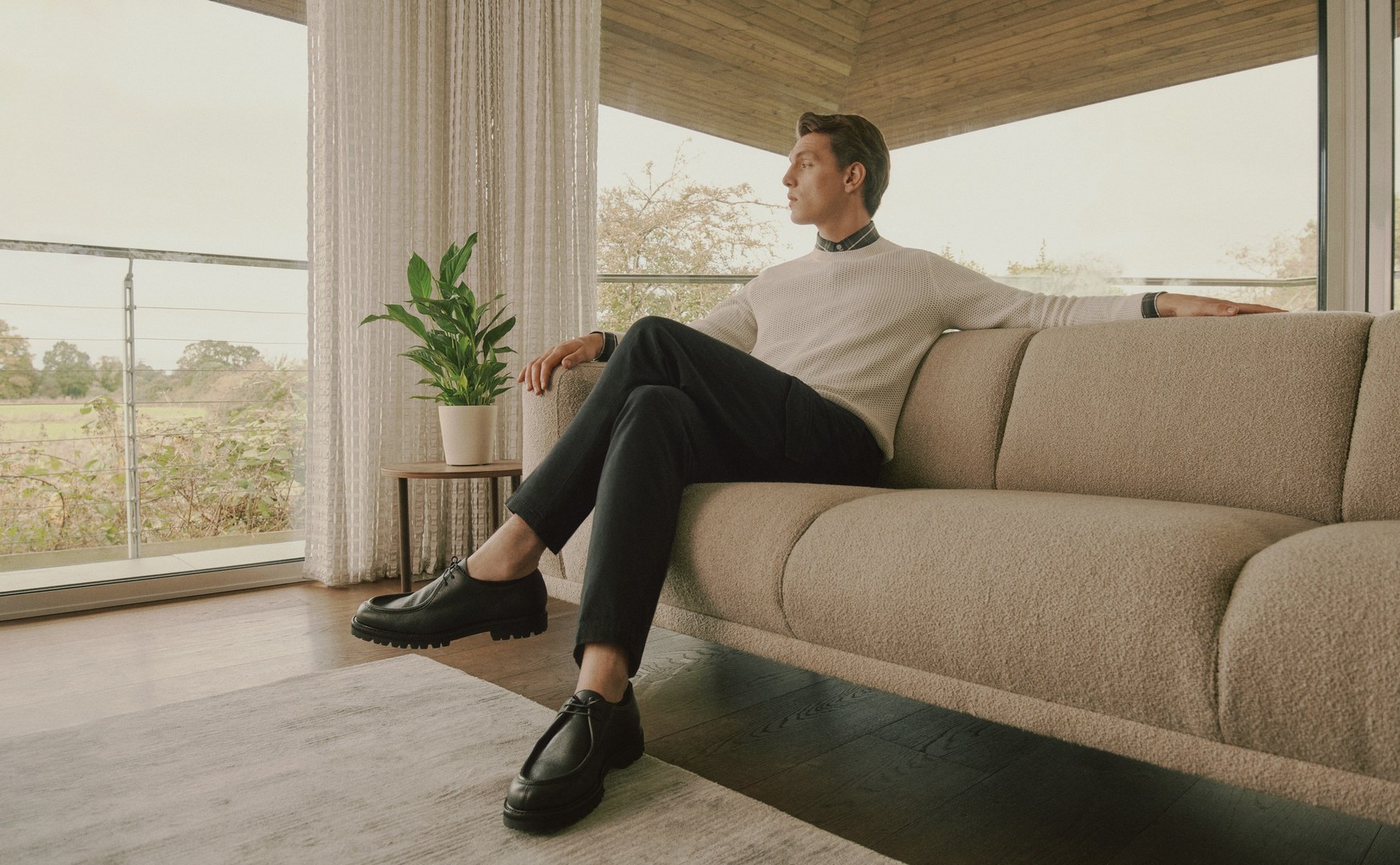 Adult male relaxes on beige couch in modern living room. Natural light streams through window, casting soft shadows. Stylish, comfortable lifestyle.