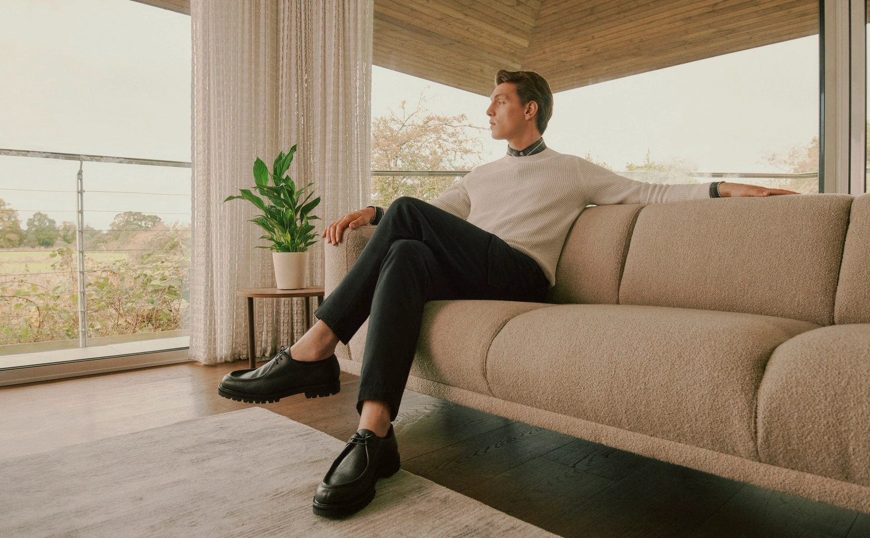 Man in cream sweater and dark trousers seated on a textured beige sofa in a modern interior by Sam Wilson