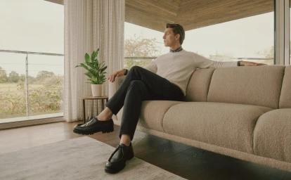 Man in cream sweater and dark trousers seated on a textured beige sofa in a modern interior by Sam Wilson
