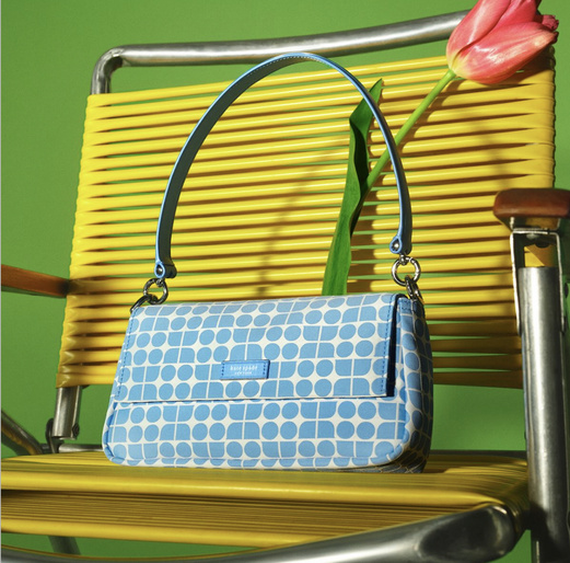 Light blue Kate Spade handbag on a yellow metal chair with a pink tulip and green background, product photography.
