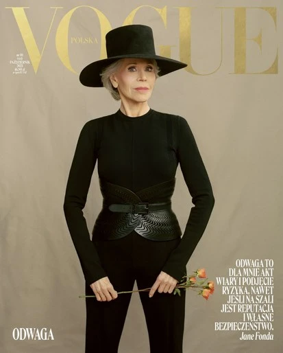 Jane Fonda on Vogue Polska cover, wearing black hat and outfit, holding light orange roses, tan studio background, direct gaze fashion shot.