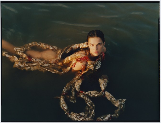 A dark-haired woman in water wearing an iridescent scaly garment designed by Bryn Bowen