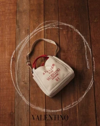 Valentino canvas atelier handbag resting on a weathered wooden plank floor encircled by white chalk drawing