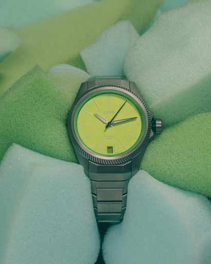 Oris watch with a stainless-steel band and a neon-yellow face nestled into a background of soft-green foam cubes, showcasing its design and color.