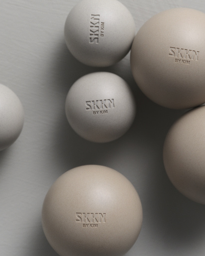 Several SKKN BY KIM spherical containers in beige and white tones arranged on a neutral surface in a product shot.