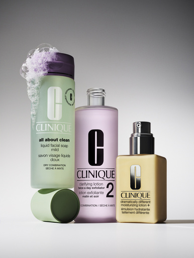 Three Clinique skincare bottles are displayed in a studio setting, featuring soap, lotion, and moisturizer, highlighted by neutral background.