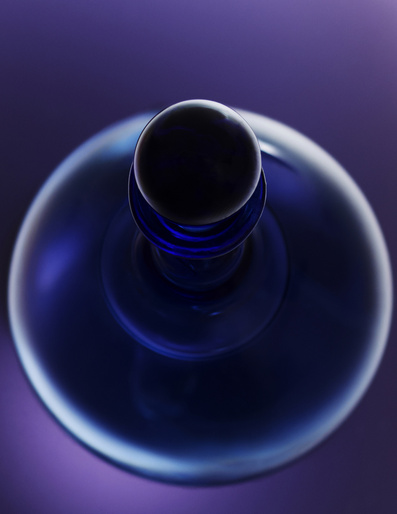 Elevated view of a sleek blue perfume bottle with a round black cap, set against a soft purple background, creating a modern, minimalist aesthetic.