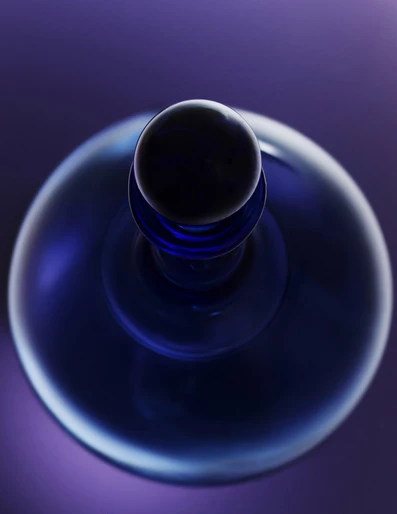 Elevated view of a sleek blue perfume bottle with a round black cap, set against a soft purple background, creating a modern, minimalist aesthetic.