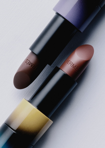 Two luxury lipstick tubes with embossed branding set against a clean white and light grey studio background.