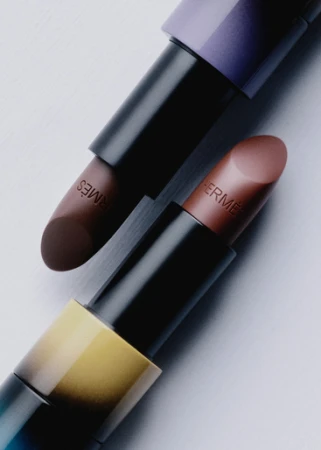 Two luxury lipstick tubes with embossed branding set against a clean white and light grey studio background.