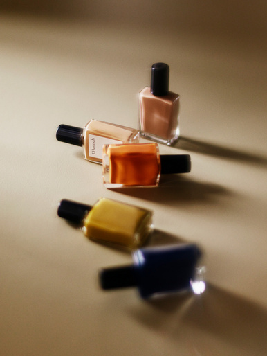 Five colorful nail polish bottles with black caps arranged on a tan surface, with visible brand labeling on one of the bottles.
