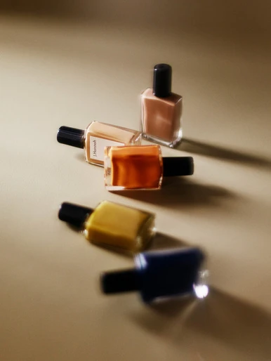 Five colorful nail polish bottles with black caps arranged on a tan surface, with visible brand labeling on one of the bottles.