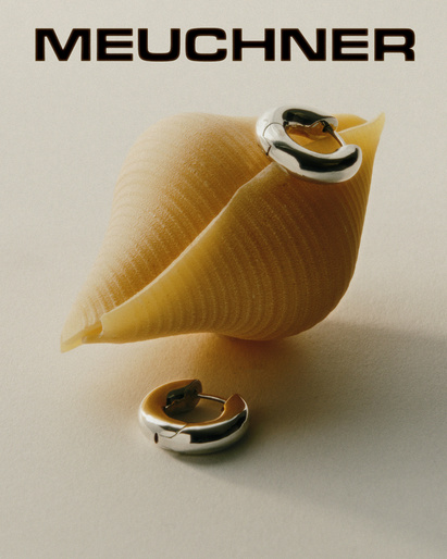 Earrings displayed with shell-shaped pasta on a cream-colored surface, with the brand name MEUCHNER visible at the top.