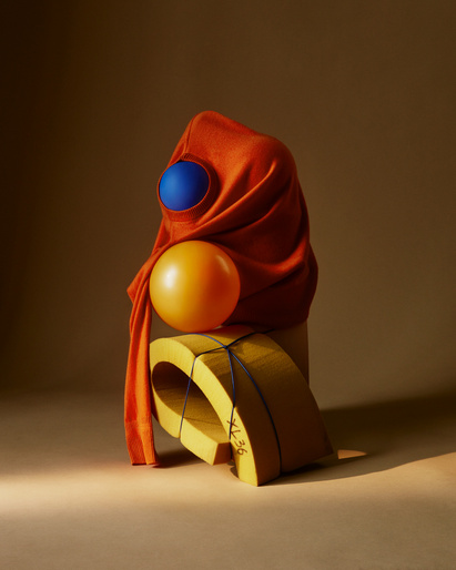 Still life shot featuring stacked geometric shapes, including yellow foam arch, orange draped fabric, and blue & yellow spheres in warm studio light.