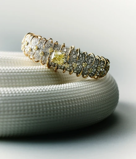 Elegant diamond-encrusted gold bangle bracelet on a textured white surface, highlighted by studio lighting for a luxury jewellery advertisement.