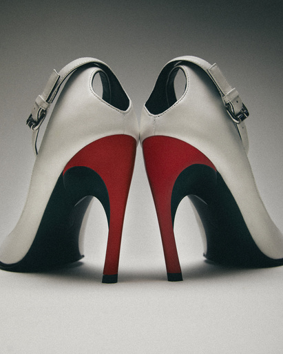 Back view of two white, red, and black high-heeled pumps on a white surface. Straps with buckles are visible on the shoes.