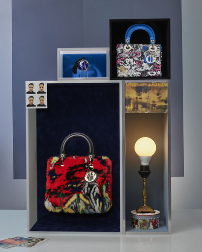 Still life of red, white and black patterned Dior handbags displayed in a white and grey shelving unit with a lamp and portrait.