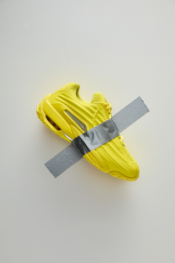 Yellow athletic shoe with duct tape strip on a white background showcasing a fusion of sports and art, blending color and texture.