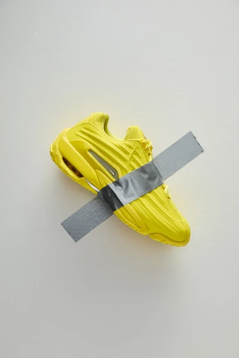 Yellow athletic shoe with duct tape strip on a white background showcasing a fusion of sports and art, blending color and texture.