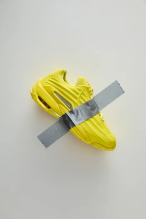 Yellow athletic shoe with duct tape strip on a white background showcasing a fusion of sports and art, blending color and texture.
