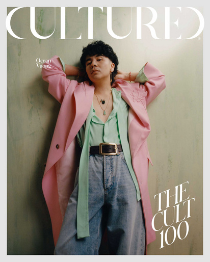 Magazine cover featuring a person with dark hair wearing a pink coat, light-green shirt, blue jeans and a belt, posing in front of a wall.