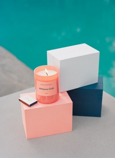 A lit candle sits on a pink box, next to matches, with a blue box and white box in the background against a blue pool.