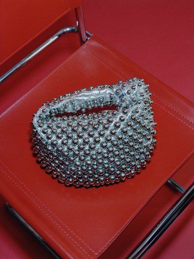Silver beaded purse sitting on a red chair in a studio setting. The purse is the primary focus of the image with a red background.