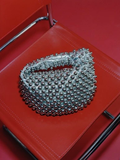 Silver beaded purse sitting on a red chair in a studio setting. The purse is the primary focus of the image with a red background.