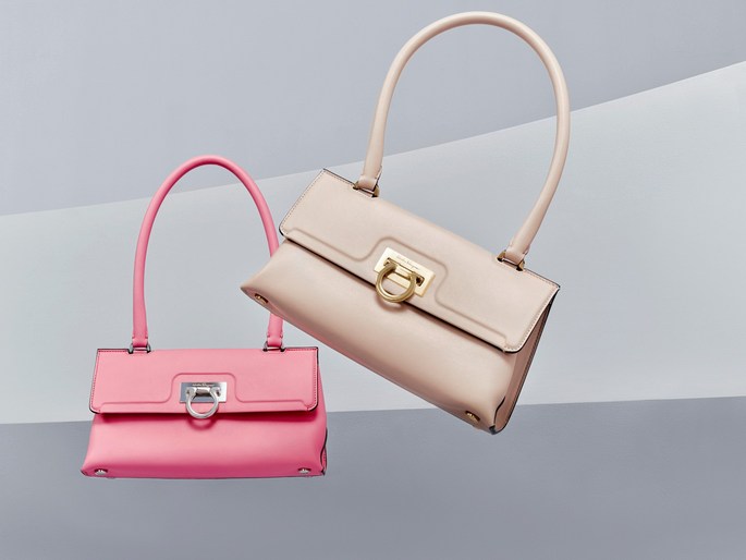 Two leather handbags in pink and light beige with curved handles are floating in front of a grey and white geometric background.