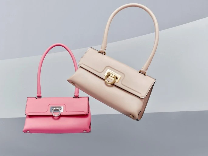 Two leather handbags in pink and light beige with curved handles are floating in front of a grey and white geometric background.