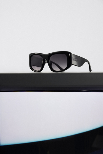 Studio shot of sleek black sunglasses with gradient lenses, resting on a black shelf against a bright white backdrop.