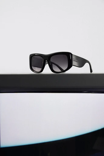 Studio shot of sleek black sunglasses with gradient lenses, resting on a black shelf against a bright white backdrop.
