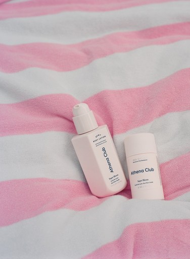 Athena Club lotion and deodorant on pink and white striped towel. Beauty and personal care product photography with soft lighting.