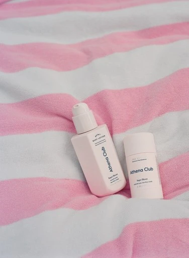 Athena Club lotion and deodorant on pink and white striped towel. Beauty and personal care product photography with soft lighting.