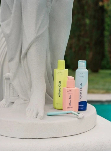 Athena Club product assortment featuring body lotion, shave cream, and razor displayed on a white statue against an outdoor setting.