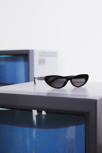 Sunglasses with black frames and dark lenses rest on a gray cube in front of another cube with a bright blue interior.
