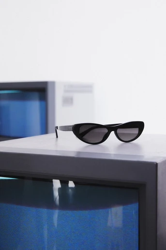 Sunglasses with black frames and dark lenses rest on a gray cube in front of another cube with a bright blue interior.
