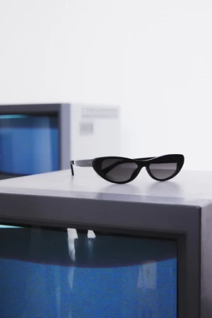 Sunglasses with black frames and dark lenses rest on a gray cube in front of another cube with a bright blue interior.