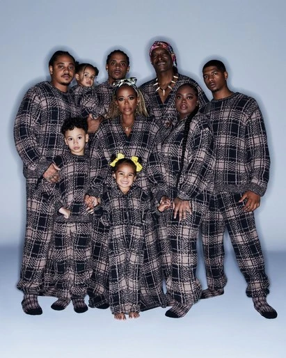 A large group of ten people, including adults and children, pose in matching brown-and-black plaid pajamas against a light blue background.