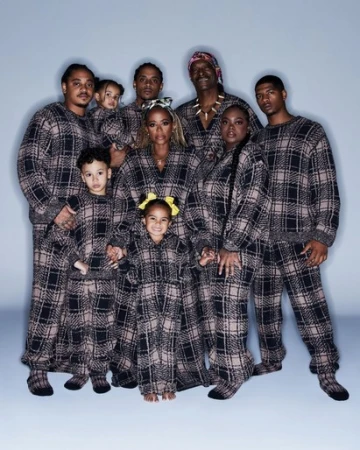 A large group of ten people, including adults and children, pose in matching brown-and-black plaid pajamas against a light blue background.