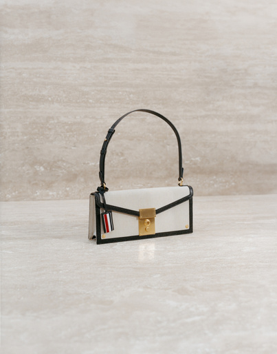 Elegant white leather handbag with a black handle and gold clasp, displayed against a beige marble backdrop in a studio setting.