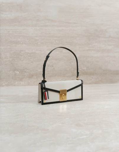 Elegant white leather handbag with a black handle and gold clasp, displayed against a beige marble backdrop in a studio setting.