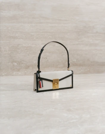 Elegant white leather handbag with a black handle and gold clasp, displayed against a beige marble backdrop in a studio setting.